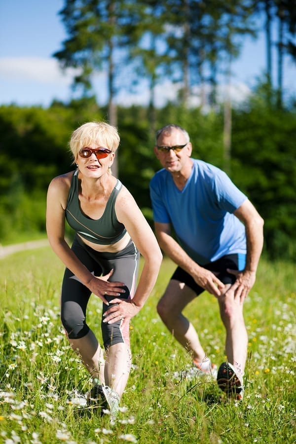 Mature or senior couple in jogging gear doing sport and physical exercise outdoors, stretching and gymnastics